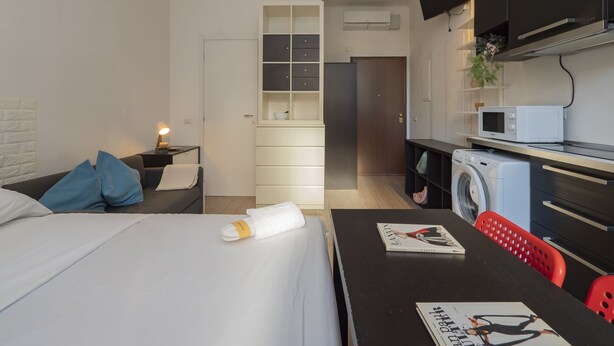 Een moderne hotelkamer met een bed, een bureau met een tijdschrift, een wasmachine en een televisie boven de balie.