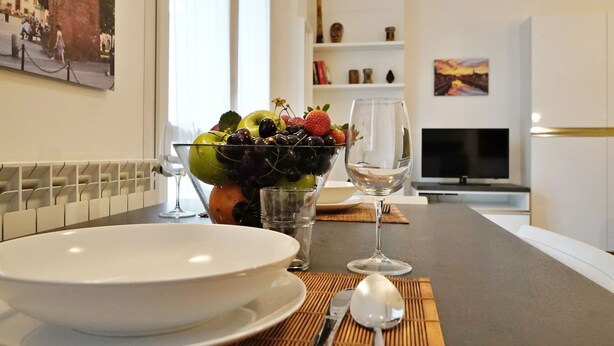 Una mesa de comedor con un bol de fruta, una copa de vino y cubiertos.