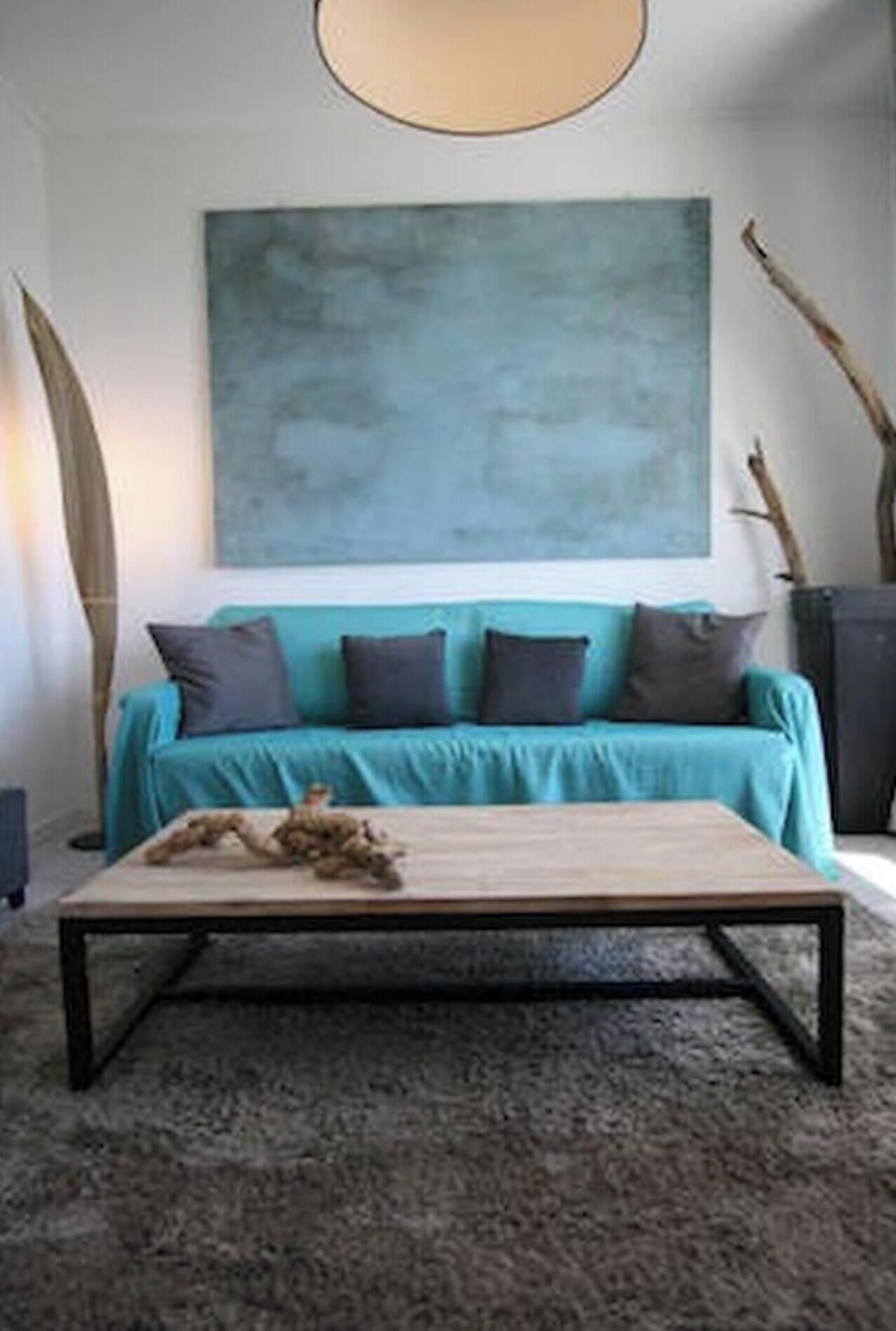 Un salon moderne avec un canapé de couleur turquoise, une table basse et un grand tableau abstrait accroché au mur.