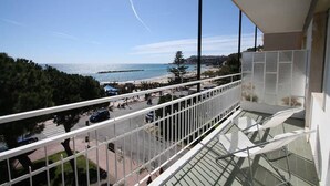 Un balcon avec vue sur la mer et la plage, une balustrade en verre et un ciel dégagé.