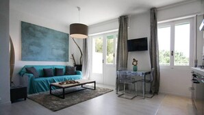 Un salon moderne avec un canapé de couleur turquoise, une table basse, un grand tableau abstrait, un téléviseur et un coin repas comprenant une table et des chaises en verre.