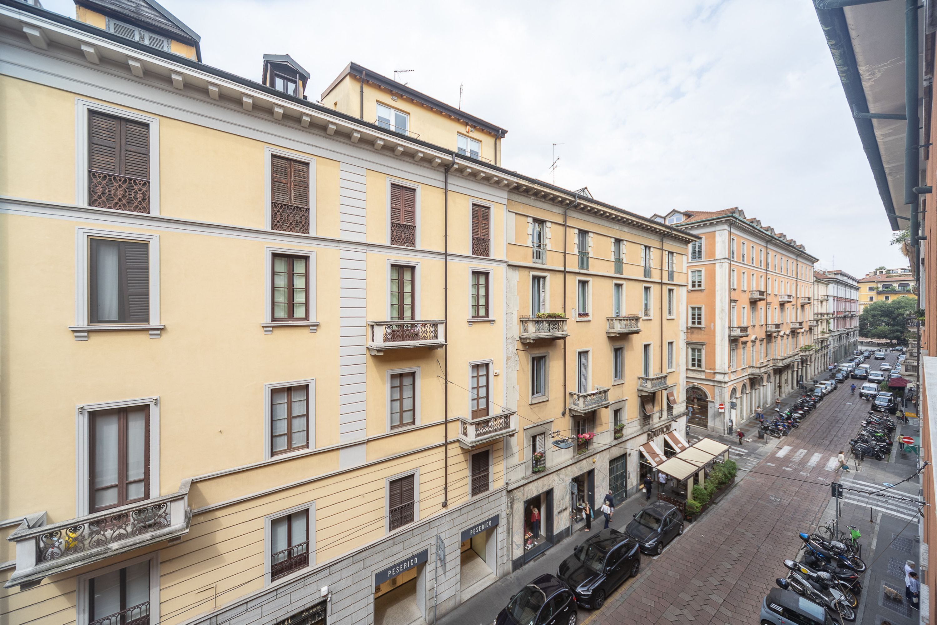 A row of yellow buildings with balconies, parked cars, and a clear street.