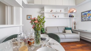Un comedor con una mesa redonda dispuesta para cuatro personas, rodeado de paredes blancas y un sofá gris.