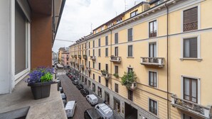 Una hilera de edificios amarillos con balcones, una calle con coches aparcados y una planta en maceta en el balcón.