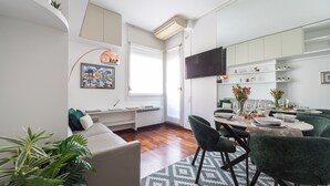 Una sala de estar moderna con un sofá, un comedor con una mesa lista para cuatro comensales, y una cocina con armarios y un televisor de pantalla plana.