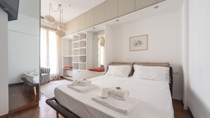 Una habitación de hotel moderna con una cama grande, una mesita de noche, un armario y una zona de estar con una silla y una pequeña mesa.