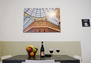 A dining area with a table set for two, a bottle of wine, and a bowl of fruit. - Candiani E2 Trilocale 2 Livelli (Milan)