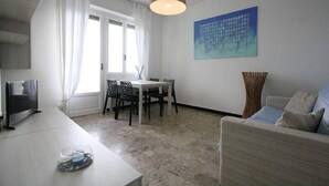 Een moderne woonkamer met een eethoek, een flatscreen televisie en een groot raam met gordijnen.