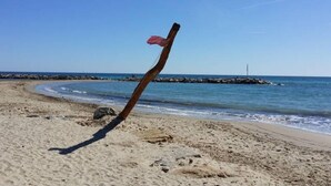 Een strand met een houten paal en een vlag, helderblauwe lucht en rustige zee.