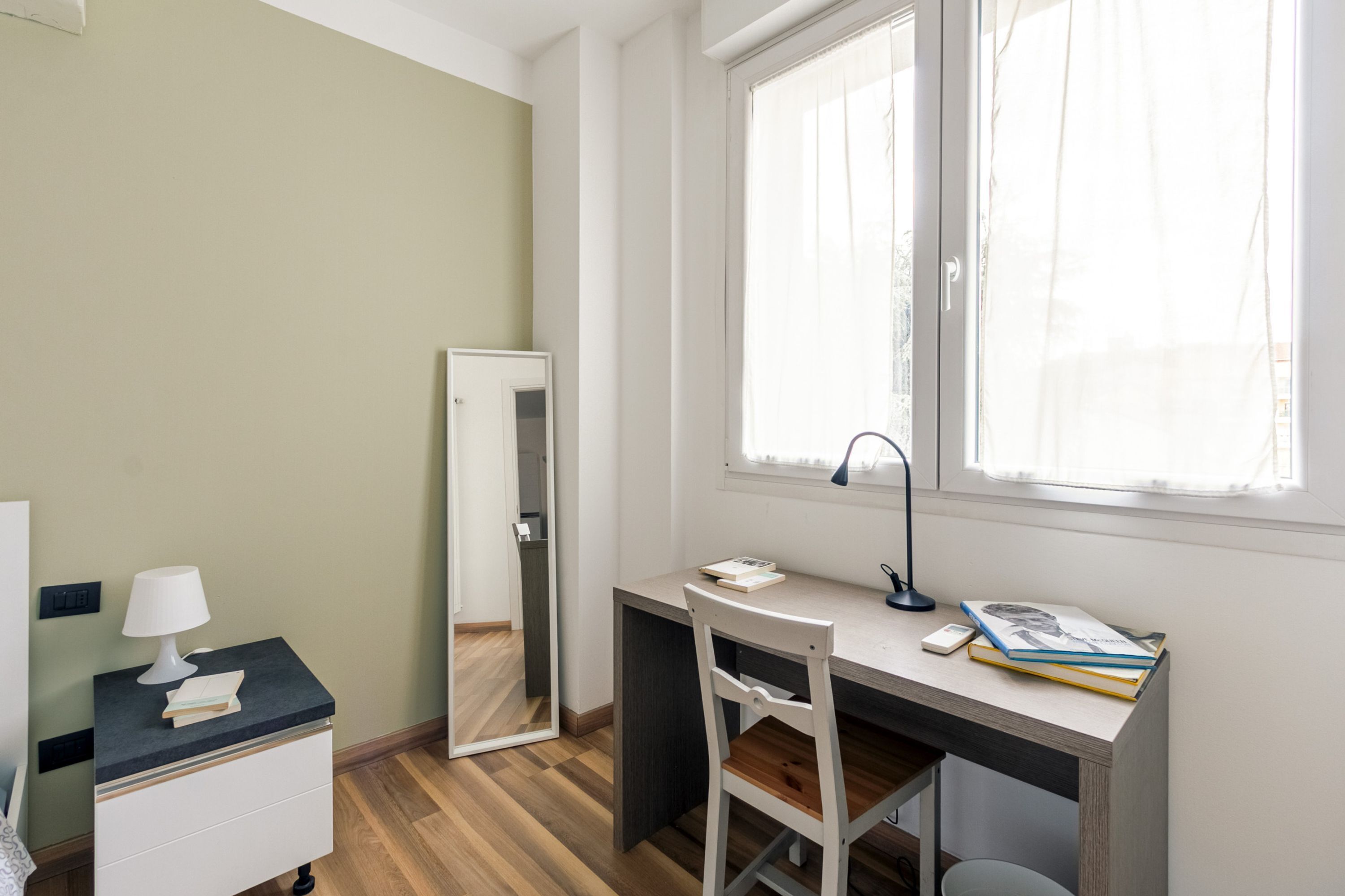 A bedroom with a bed, a bedside table, a nightstand, a desk, a chair, and a window.
