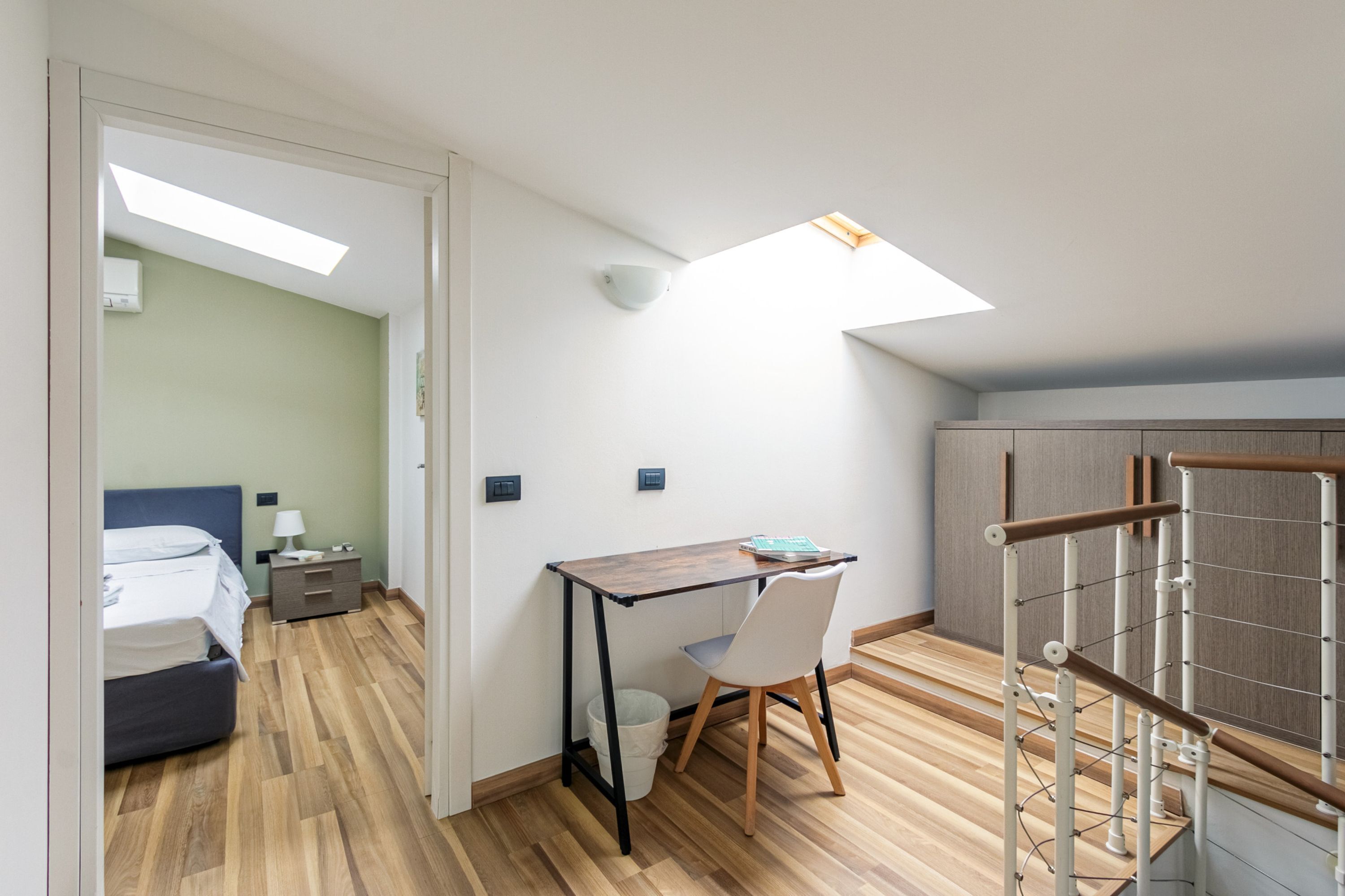 Une chambre à coucher avec un lit, une table de chevet et un bureau avec une chaise. Il y a une lucarne au-dessus du bureau.
