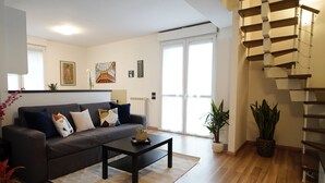 A living room with a grey sofa, a black coffee table, and a staircase with wooden steps. - Candiani Building - Modern 2BR Apartment Steps From Bovisa Politecnico (Milan)