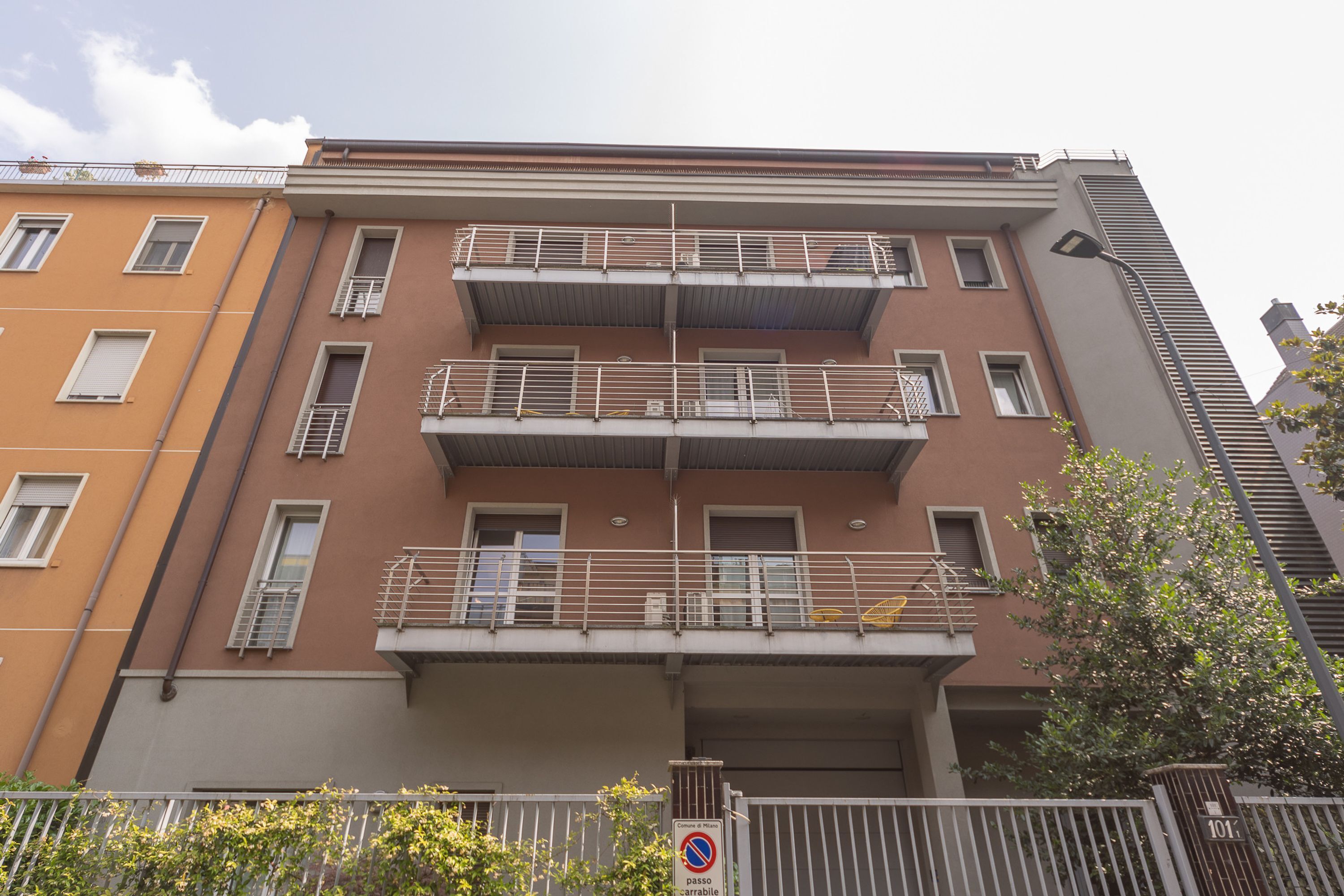 Un edificio residencial de varios pisos con balcones, un letrero de no estacionamiento y una reja.