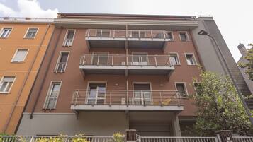 Un edificio residencial de varios pisos con balcones, un letrero de no estacionamiento y una reja.