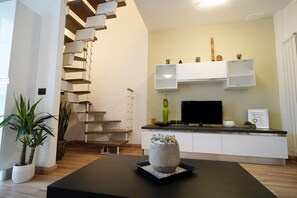 A modern living room with a staircase, a flat-screen TV, and minimalist decor. - Candiani Building - Modern 2BR Apartment Steps From Bovisa Politecnico (Milan)
