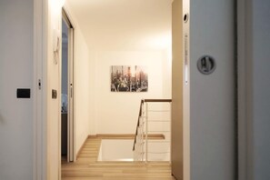 Een gang met een houten vloer, een witte deur en een aan de muur hangend schilderij.