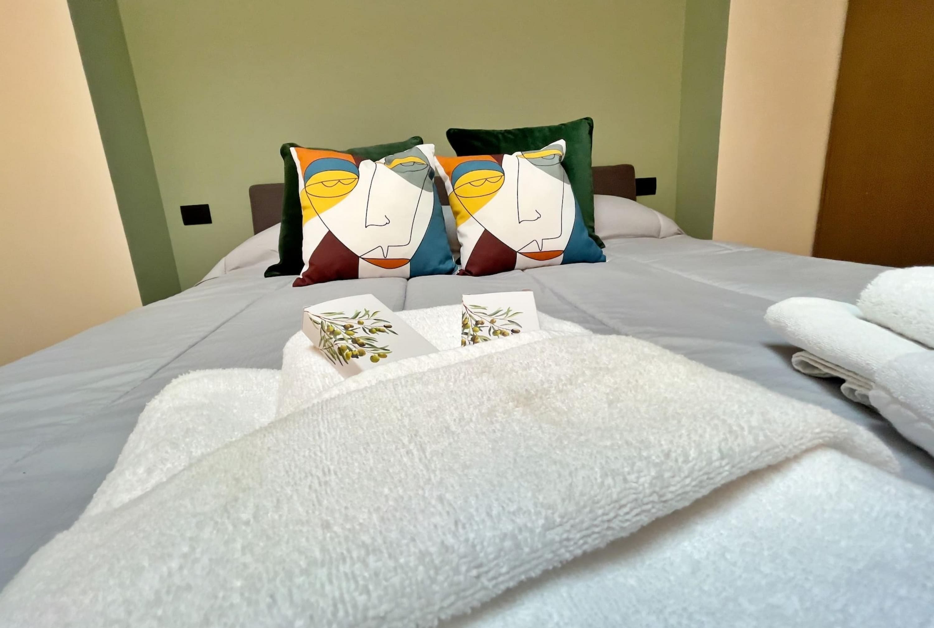 Un lit bien fait, avec du linge de lit blanc et des coussins décoratifs, une serviette blanche pliée et une petite plante décorative posée sur le lit.
