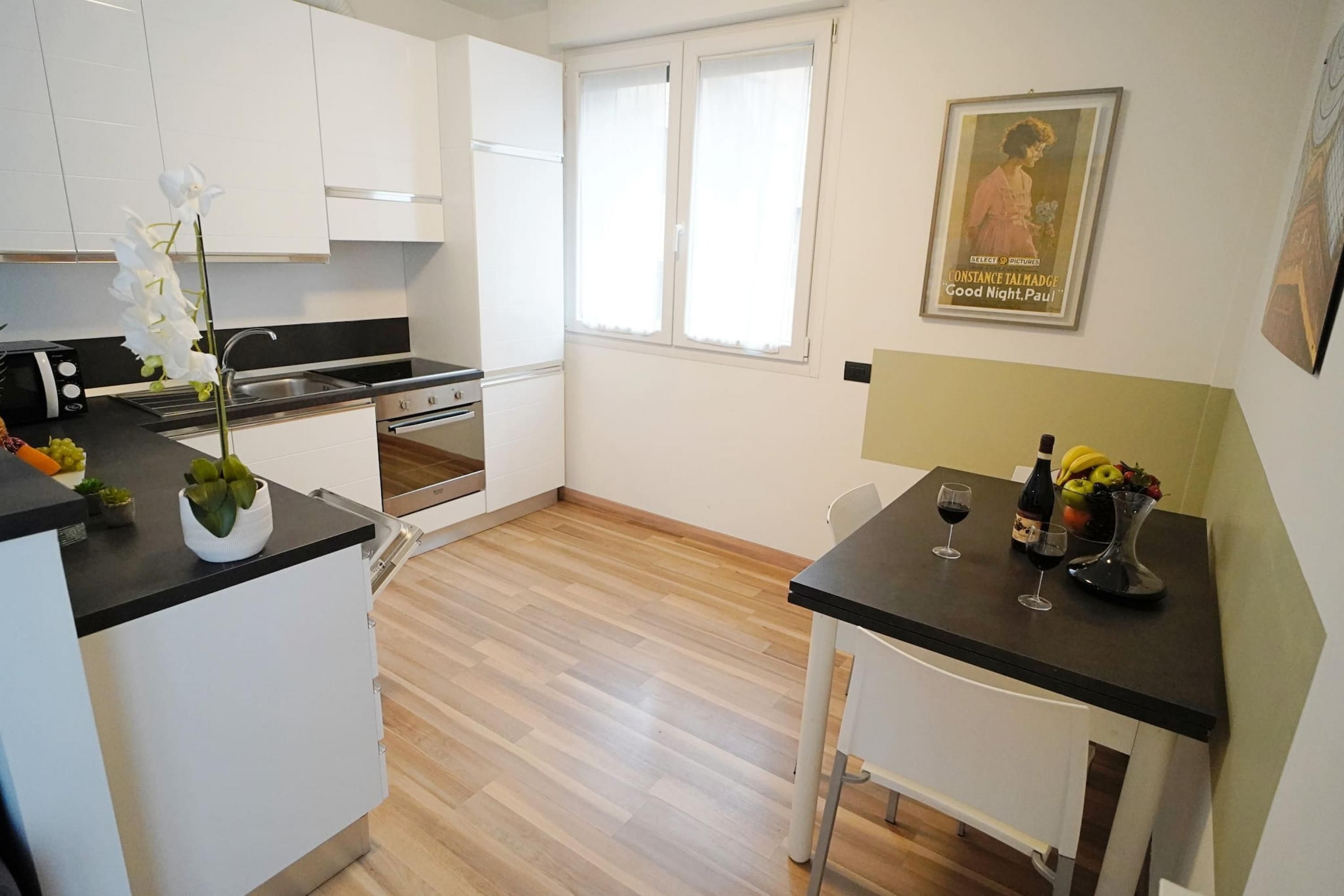 Uma cozinha moderna com armários brancos, bancada preta e uma área de refeições com mesa e cadeiras.