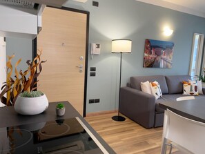 A modern living room with a grey sofa, a small table with a plant, a floor lamp, and a painting on the wall. - Candiani B2 Bilocale (Milan)