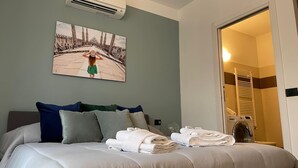 A hotel room with a bed, a painting, a bathroom with a towel rack, and an air conditioning unit. - Candiani B2 Bilocale (Milan)
