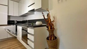 A modern kitchen with white cabinets, a microwave, a stove, and a decorative plant in a woven pot. - Candiani B2 Bilocale (Milan)