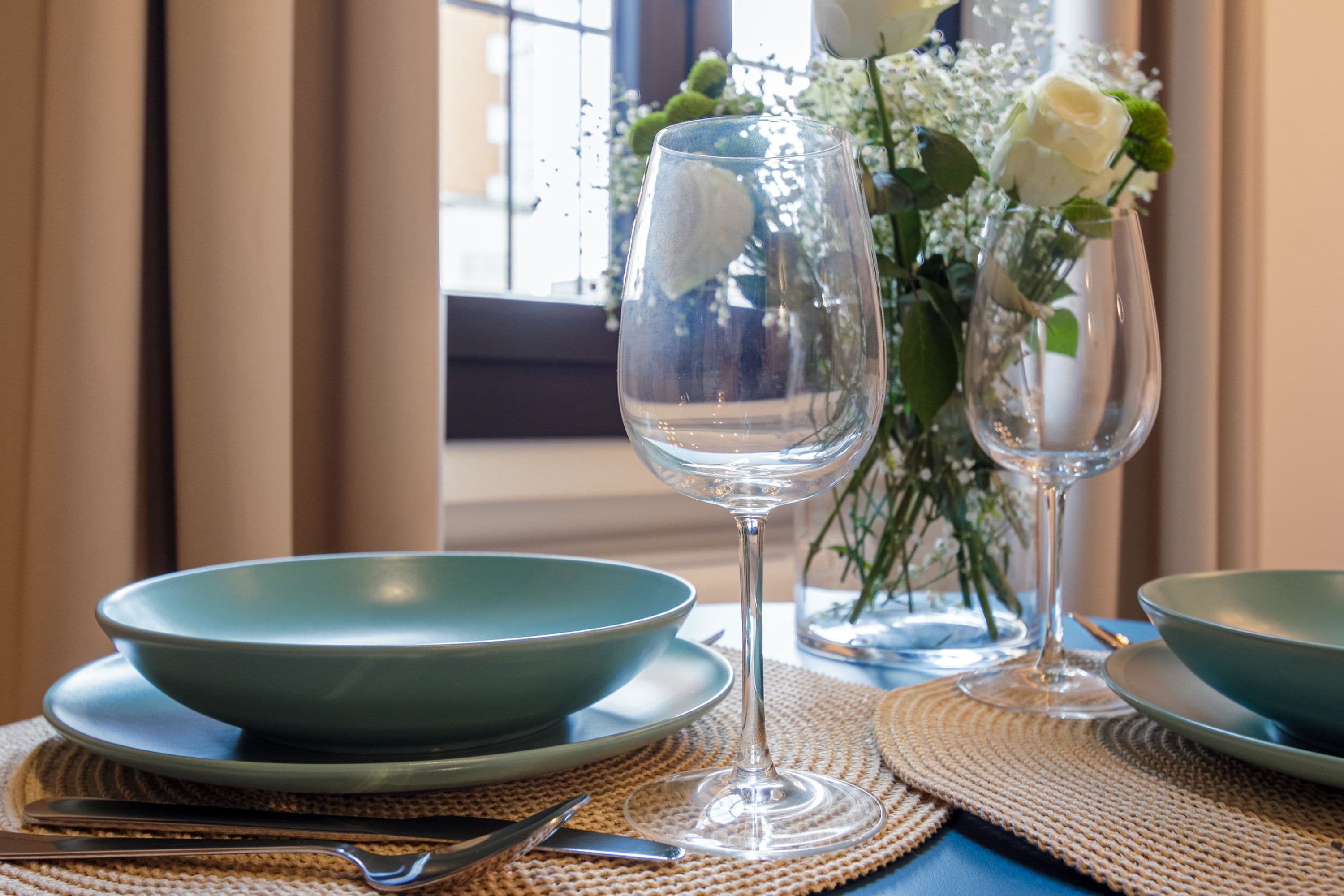 Een eettafel met een helder glas, een groene schaal en een vaas met witte bloemen.