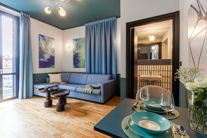 A modern living room with a blue sofa, a coffee table, and a dining table set for two with blue plates and glasses. - Quantum 6 Proton in Milano (Milan)
