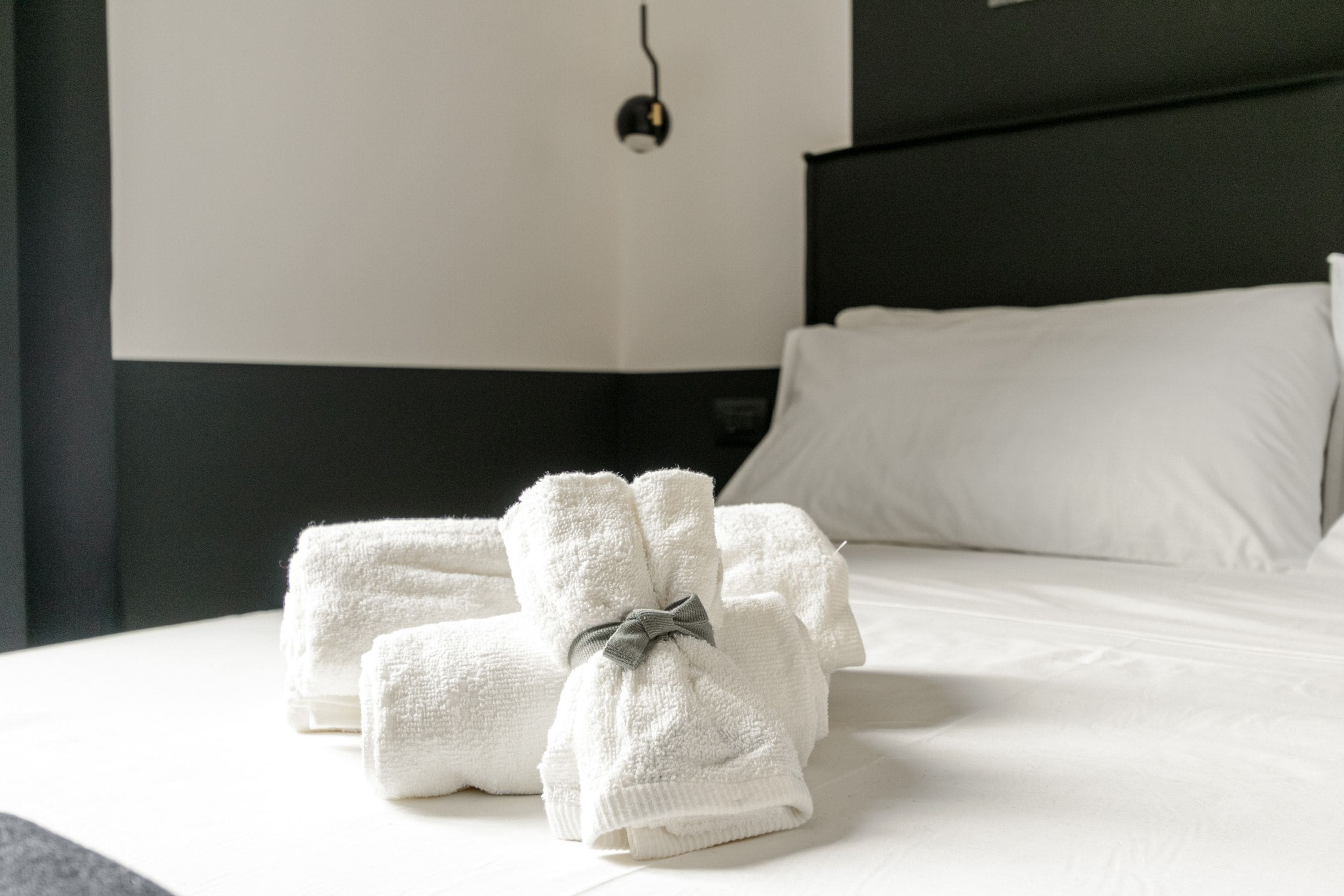 A neatly made bed with white linens and towels, a black headboard, and a single bedside lamp.