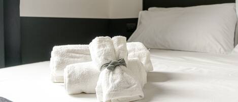 A neatly made bed with white linens and towels, a black headboard, and a single bedside lamp.