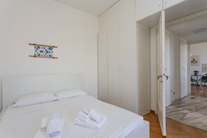 Een hotelkamer met een netjes opgemaakt bed, een klein kunstwerk aan de muur en een deur naar een eetgedeelte.
