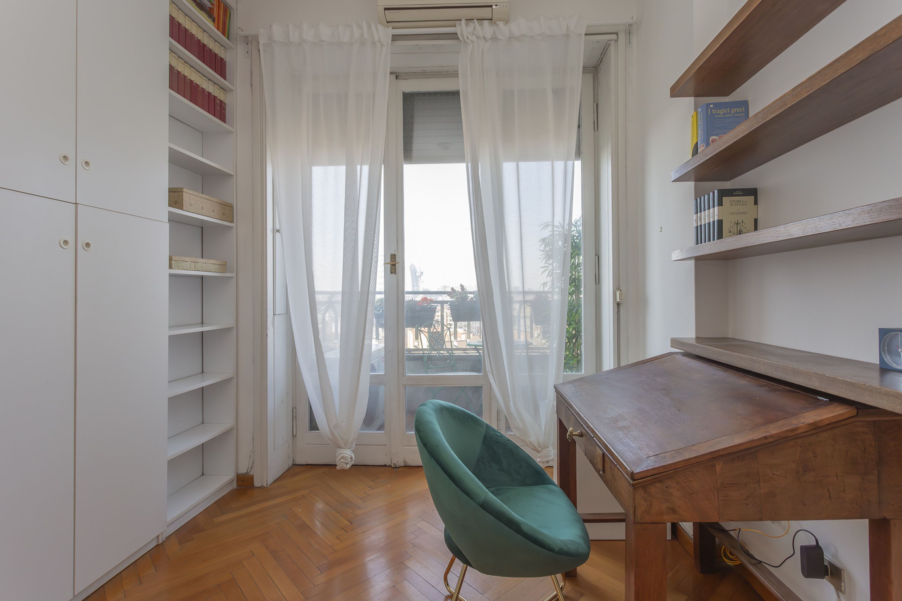 A room with a wooden desk, a teal chair, and a white bookshelf.