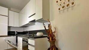 A modern kitchen with white cabinets, a microwave, a stove, and a decorative vase with dried plants. - Candiani E1 Bilocale (Milan)