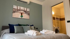 A hotel room with a bed, pillows, a wall-mounted air conditioner, and a painting of a woman in a green dress. - Candiani E1 Bilocale (Milan)
