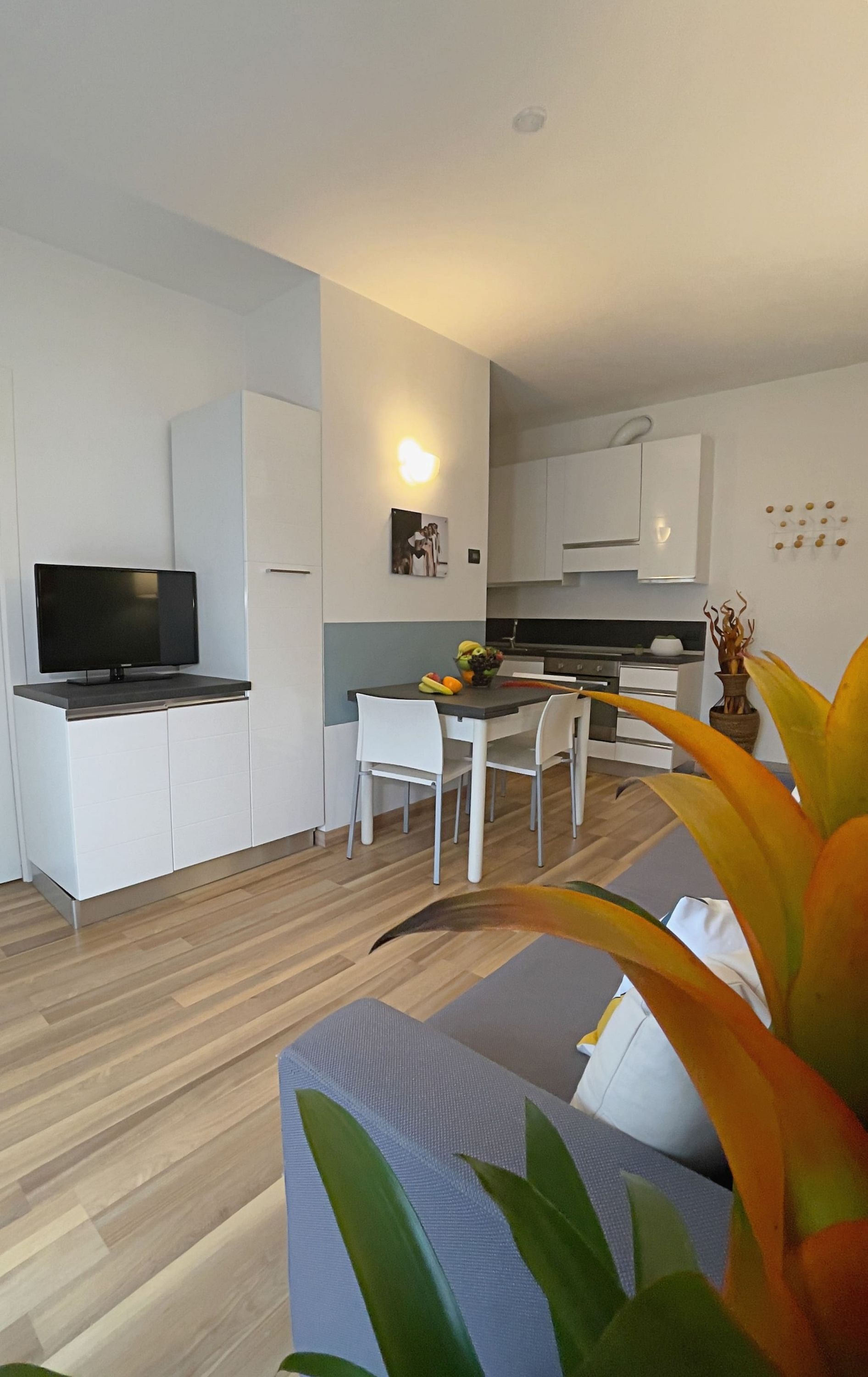 A modern kitchen with white cabinets, a dining table with chairs, and a television on a cabinet.