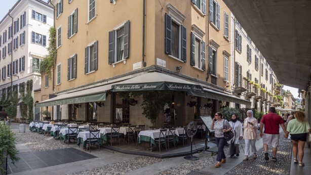 En udendørs restaurant med udendørs siddepladser, et skilt der siger "Ristorante con Pizza & Live Music", og en brostensbelagt gade.