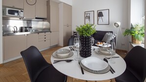 Et moderne køkken med mikrobølgeovn, komfur og vask. Der er et spiseområde med et rundt bord dækket til to personer, en sort stol og en potteplante.