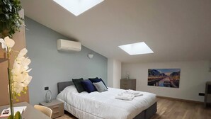A modern bedroom with a skylight, a bed with pillows, a nightstand, a desk, and a painting on the wall. - Candiani D3 Bilocale 2 Livelli (Milan)