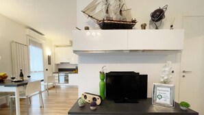 A modern kitchen with white cabinets, a black countertop, a ship model, a television, and a framed welcome sign. - Candiani D3 Bilocale 2 Livelli (Milan)