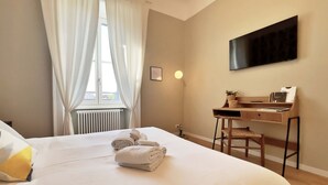 A hotel room with a large bed, a desk, a chair, a TV, and a window with curtains. - Solferino - Elegant 1bdr in Historical Building in Brera (Milan)