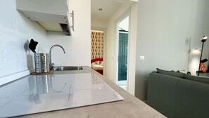 A modern kitchen with a sink, a stove, and a countertop. There is a green sofa in the living area. - Solferino - Elegant 1bdr in Historical Building in Brera (Milan)
