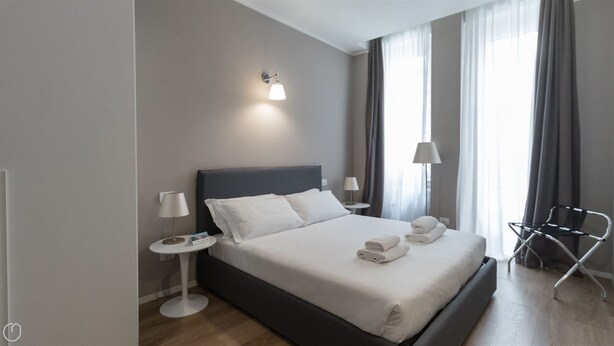Une chambre d’hôtel moderne avec un grand lit, deux tables de chevet, une chaise et une fenêtre avec des rideaux.