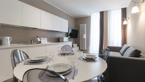 Un espace repas moderne avec une table ronde pour quatre personnes, un téléviseur à écran plat au-dessus du comptoir et un canapé à l’arrière-plan.