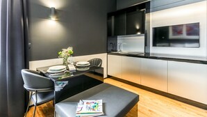 Una cocina moderna con encimera negra, armarios blancos y microondas integrado. Hay una mesa de comedor con sillas y un florero con flores.