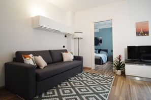 A modern living room with a dark sofa, a patterned rug, a TV, and a plant. - Candiani C2 Bilocale (Milan)