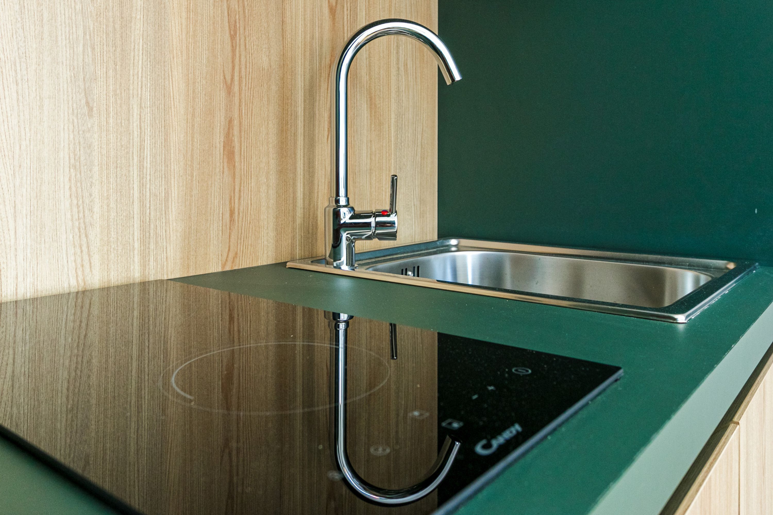 Une cuisine moderne dotée d’un évier en acier inoxydable, de meubles de rangement en bois et d’une plaque de cuisson à induction noire.
