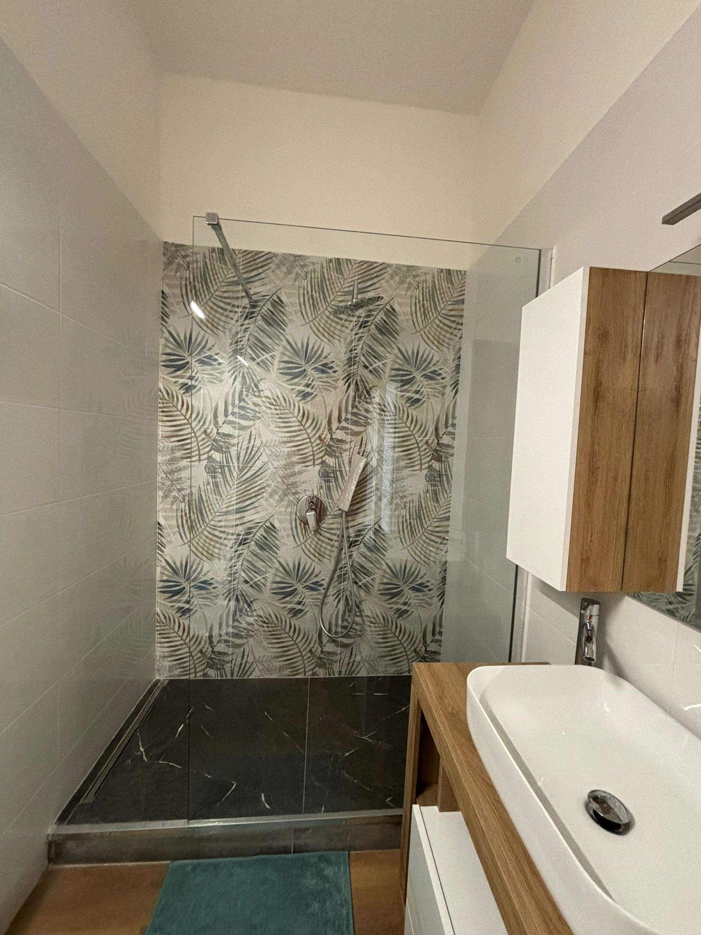 A bathroom with a shower area, a sink, and a wooden cabinet.