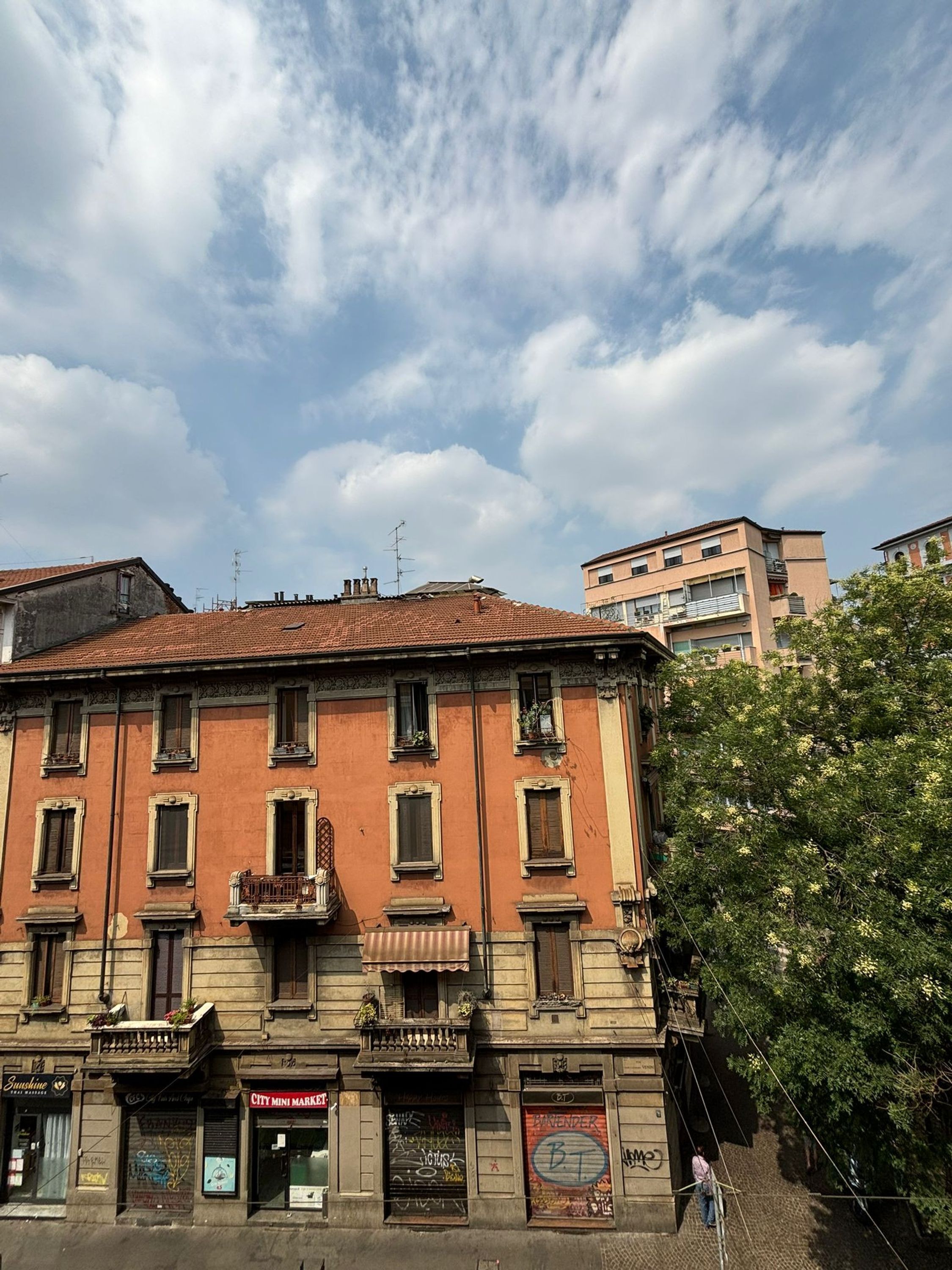 A multi-story building with a red facade, multiple balconies, and a mix of commercial and residential spaces.