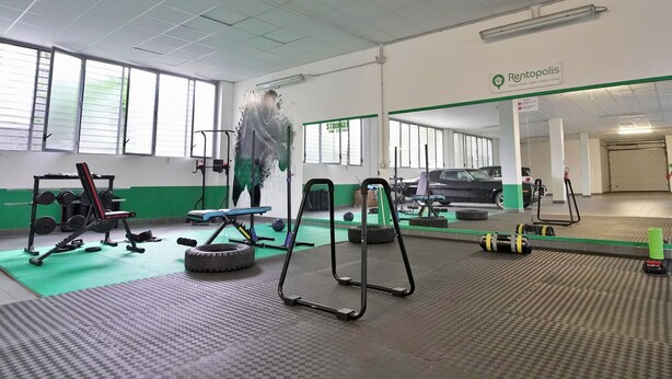 A gym with exercise equipment, a car, and a sign for Rentopolis. - Candiani F1 Bilocale (Milan)
