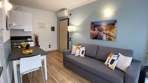 A modern living room with a grey sofa, a dining table with fruit, and a cityscape painting on the wall. - Candiani F1 Bilocale (Milan)