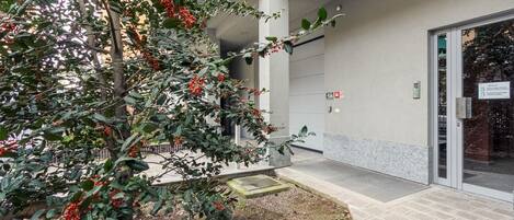 Entrada de edificio con un área exterior techada, un árbol con bayas rojas y un letrero que indica un espacio de estacionamiento para discapacitados.